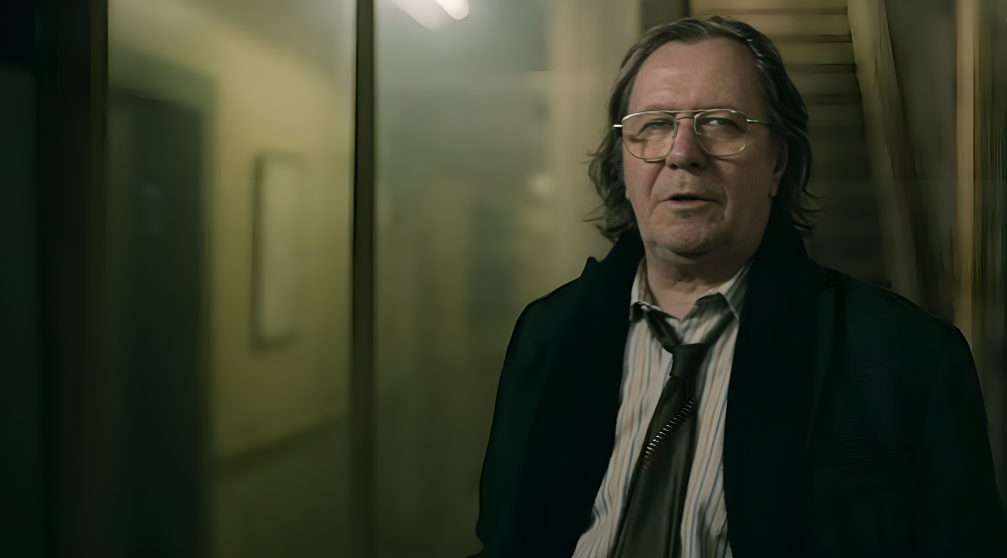 A group of British intelligence agents, led by a disheveled older man, stands in a dimly lit office filled with old files and computers, suggesting espionage and dark humor.