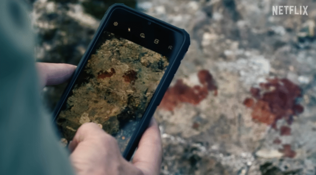 Close-up of a phone screen capturing blood evidence on rocky ground.