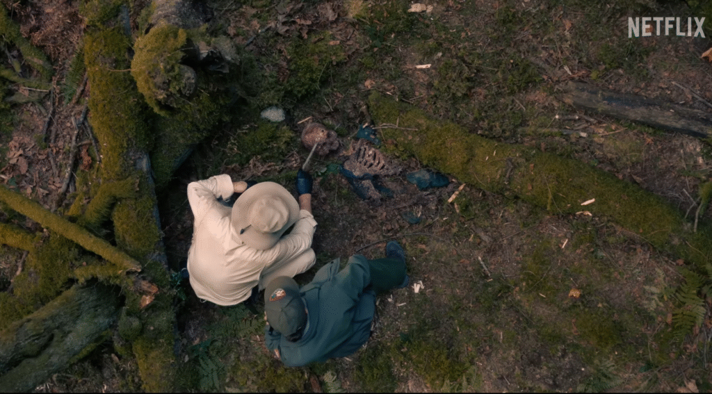 Two rangers uncover a moss-covered skeleton in the forest in Netflix’s Untamed Season 1.