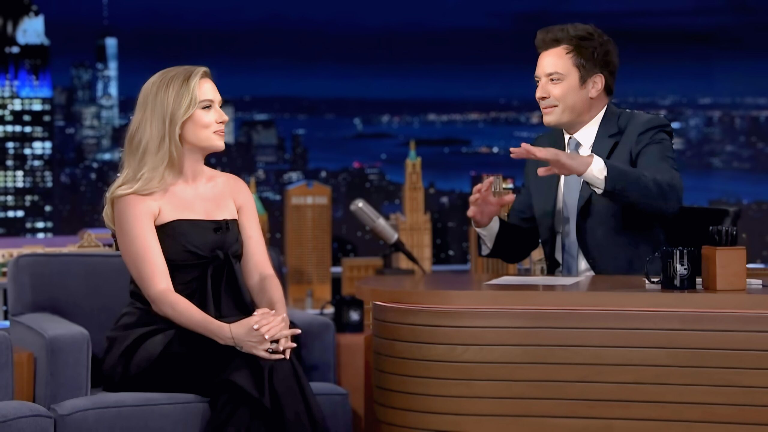 Scarlett Johansson smiling while talking to Jimmy Fallon on The Tonight Show set.