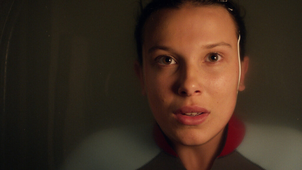 Millie Bobby Brown as Eleven looks directly at the camera while relaxing in a bathtub, promoting Stranger Things Season 5.